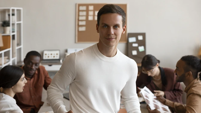 homem de branco feliz pela produtividade de sua esquipe que esta sentado atrás dele focados no trabalho