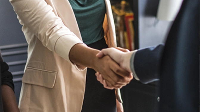 aperto de mão de uma mulher negra de terno breje e um homem branco de terno preto. Após fecharem o programa de integração de novos funcionários.