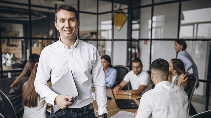 homem feliz liderando uma dinâmica de grupo que acontece atrás dele com sua equipe